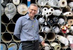 Picture of Glynn standing in front of rolls of fabric.