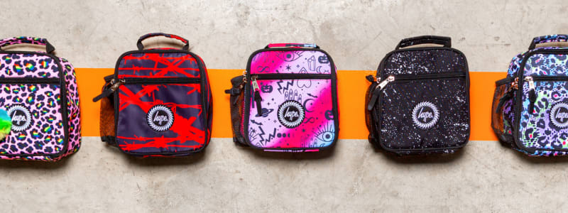 A row f mini backpacks in various designs sit on an orange line drawn on concrete.