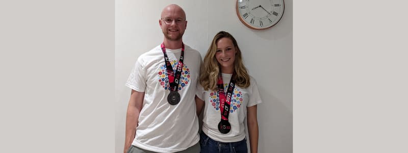 Will stands in a room next to his running partner Gaby. Both will and Gaby are wearing their London Marathon medals.