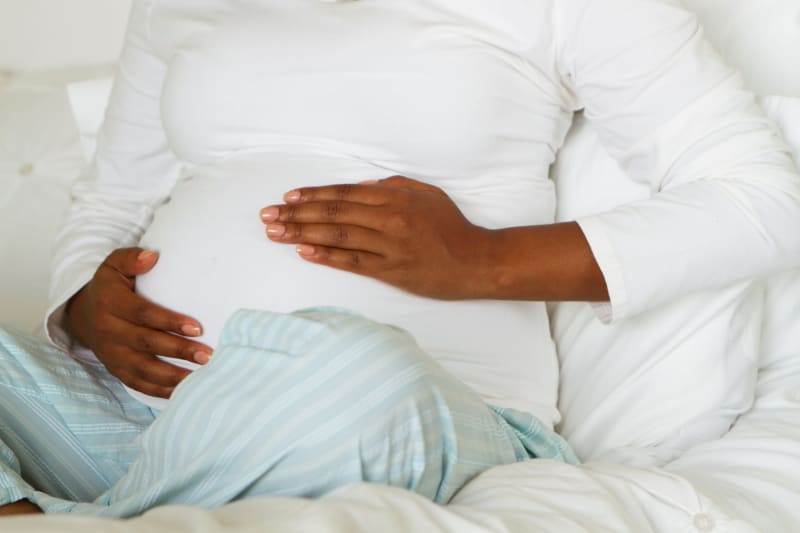 woman sitting on a bed holding her pregnant stomach.