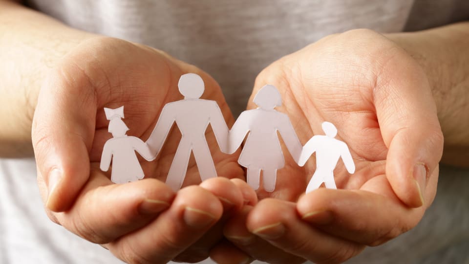 Hands holding a paper cut out family.
