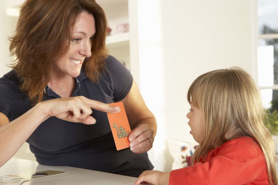 Women shows a alphabet card to a child with down syndrome, during a speech therapy session. 